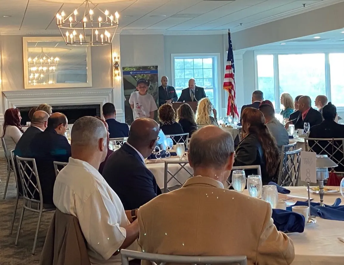 A group of people sitting at tables in front of an american flag.