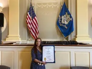 A woman holding an award in front of two flags.