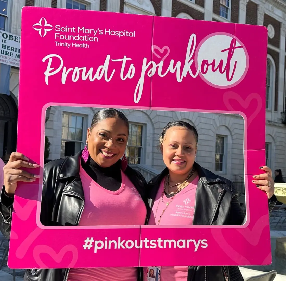 Two women smiling, holding pink out sign.