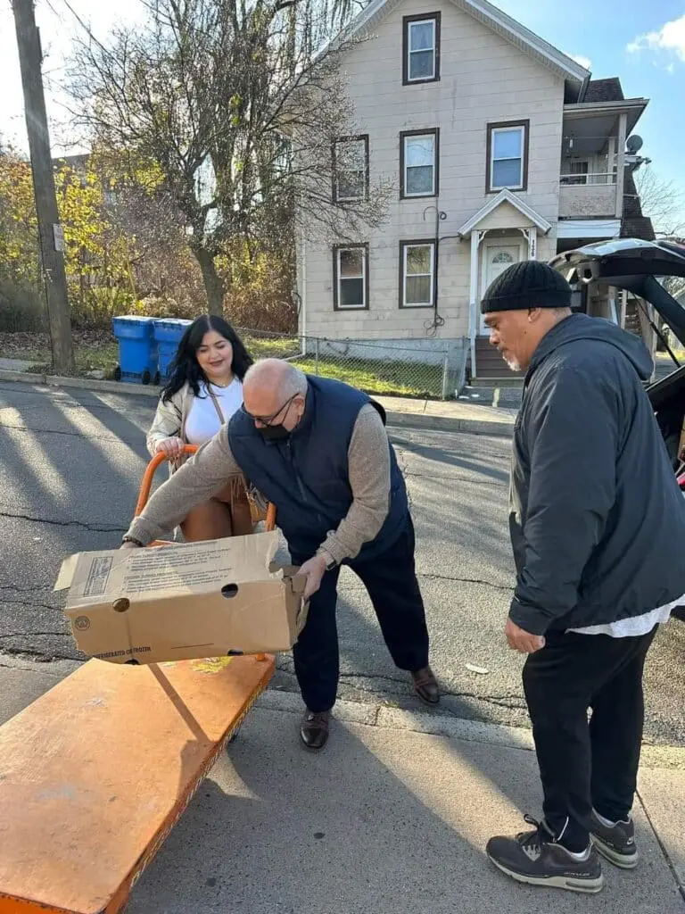 Three people loading a box onto a dolly.