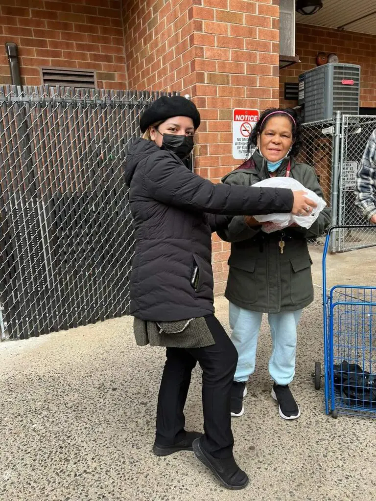 Two women wearing masks exchange food.