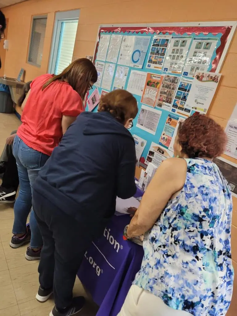 Three women looking at a bulletin board in a room.