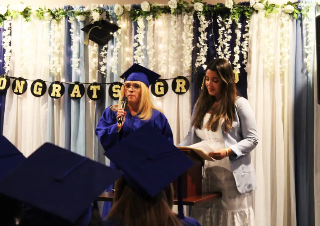 A woman in blue cap and gown speaking at a graduation.