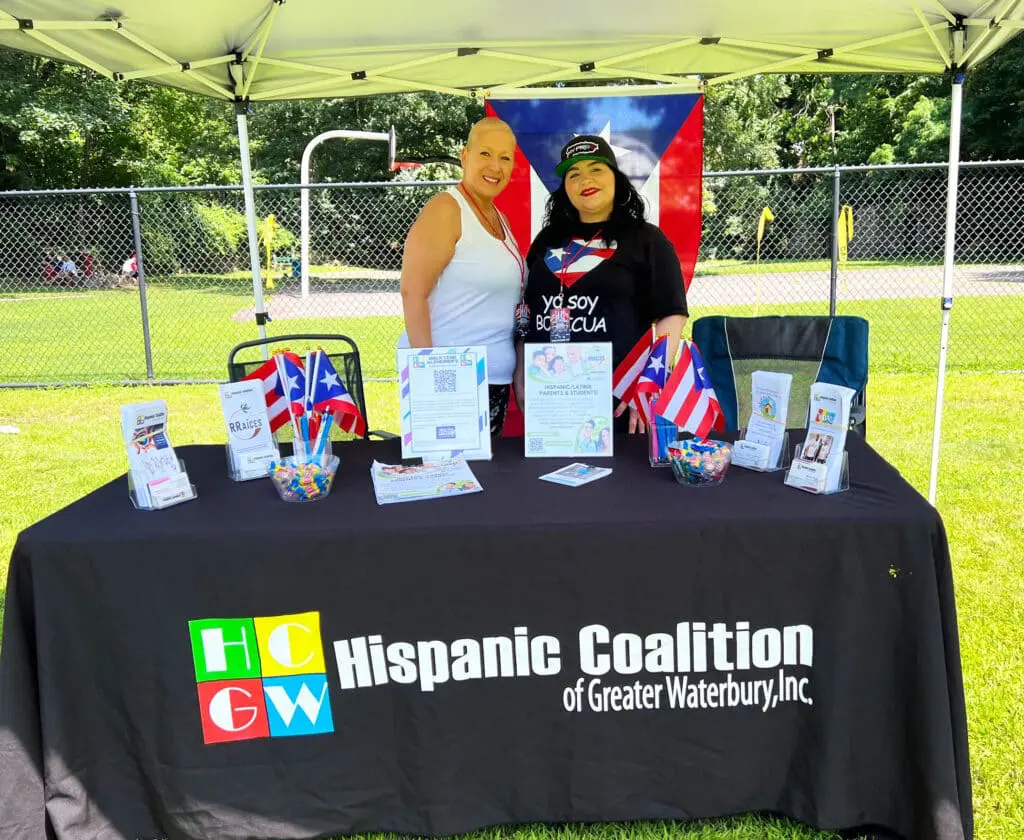 Two women standing at a table with flags and signs.