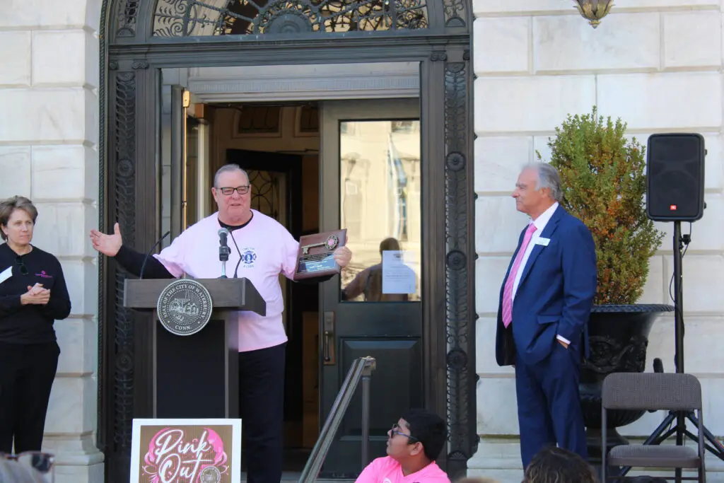 A man in pink shirt standing at podium next to two men.
