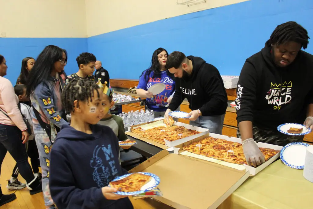 A group of people standing around pizza boxes.