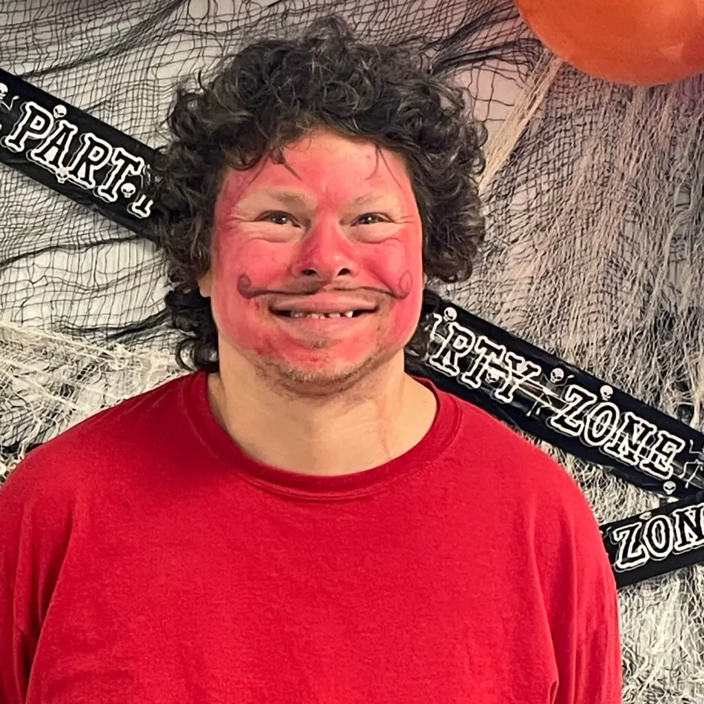A man with red face paint and curly hair.