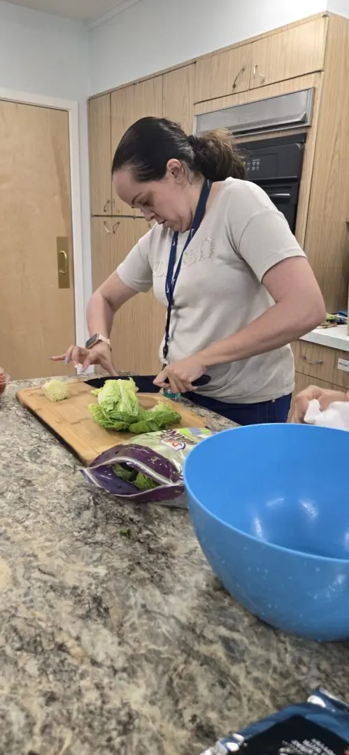 A woman cutting broccoli on top of a wooden board.