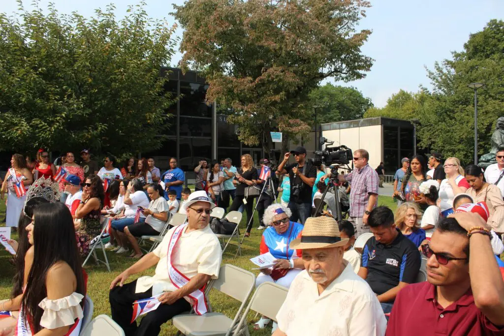 Outdoor gathering with seated and standing attendees.