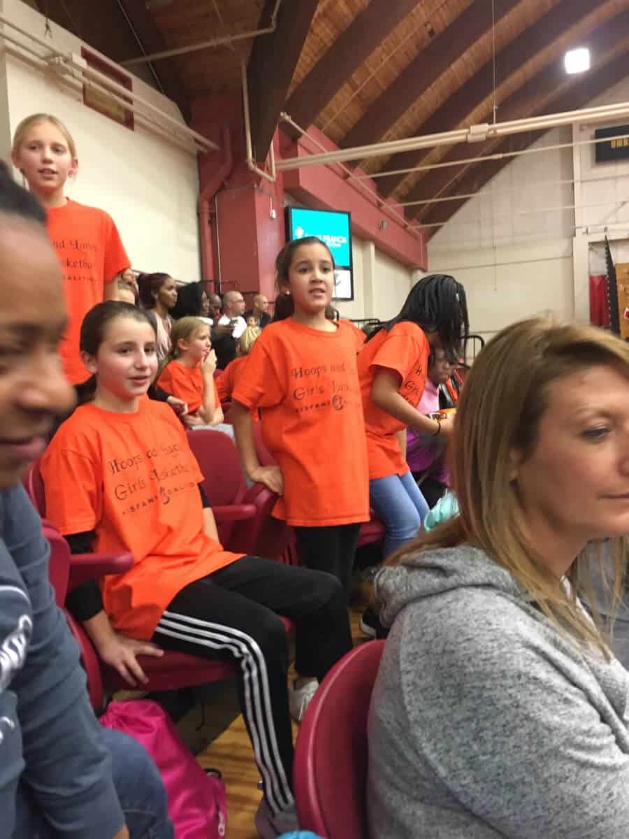 A group of young people in orange shirts sitting on chairs.