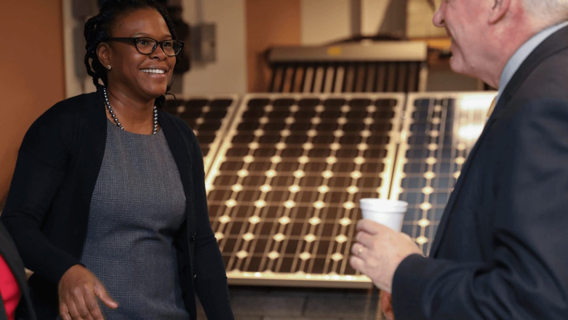 Woman in glasses smiling at man holding cup.