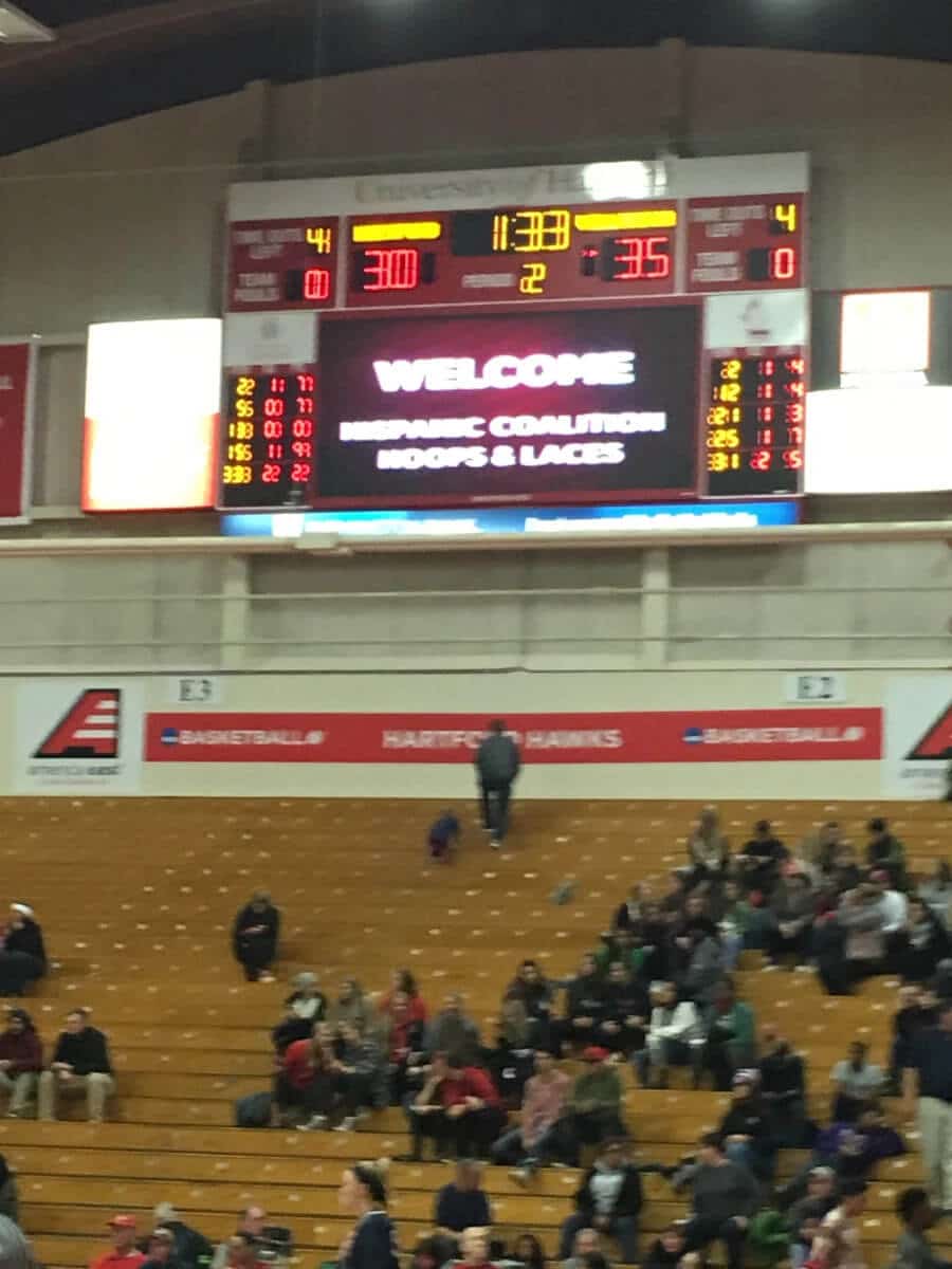 A crowd of people sitting in front of an electronic scoreboard.