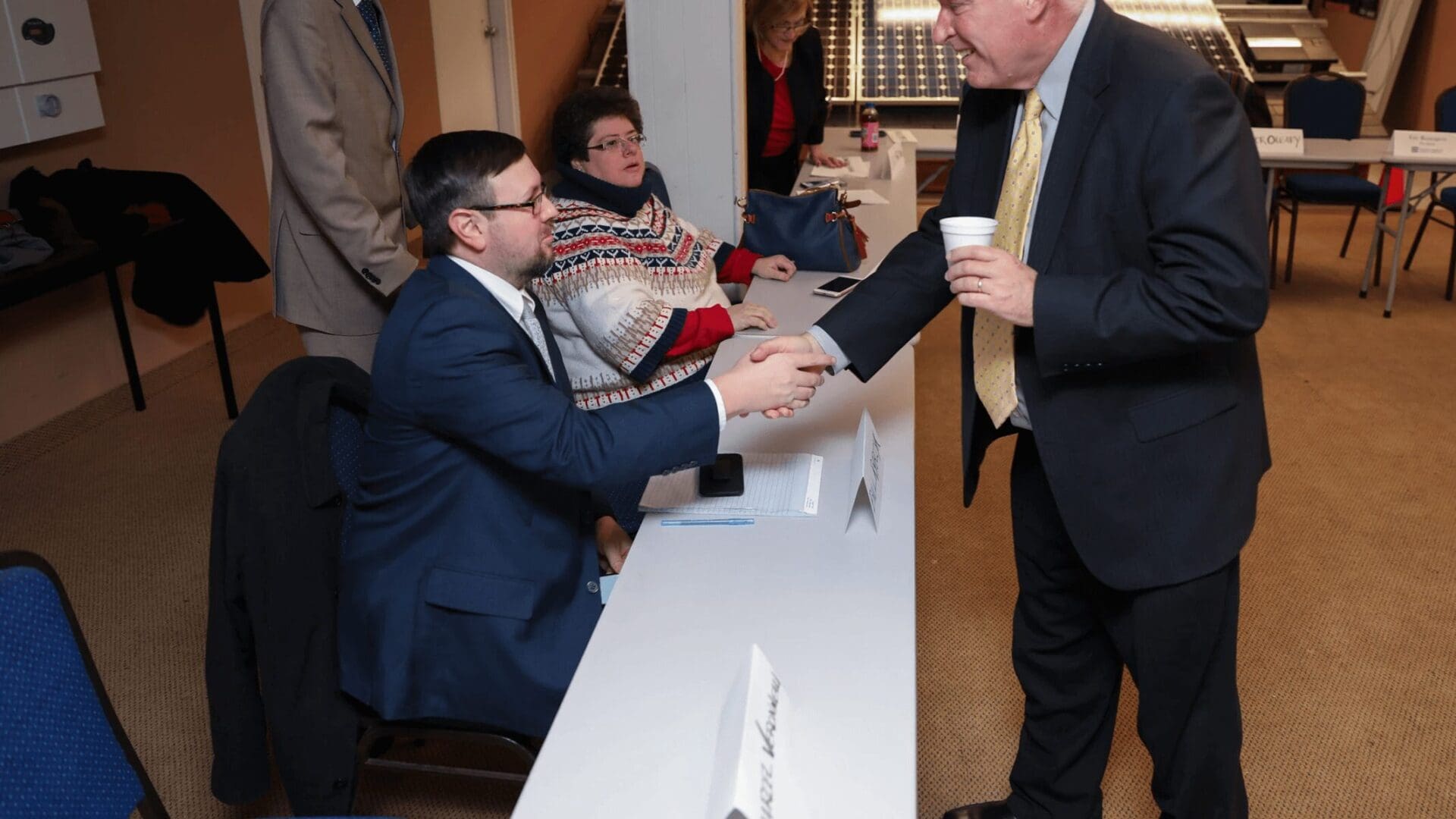 A man in a suit and tie handing his hand to another man.