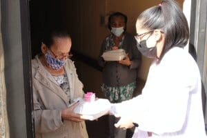 Three people wearing masks exchange food.