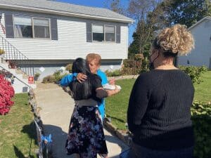 Two women hug outside a house.