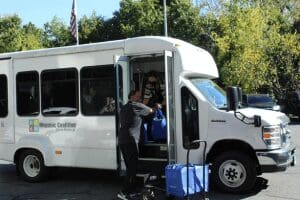 A man loading luggage into the back of a white bus.