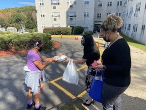 Three women exchange food outside building.