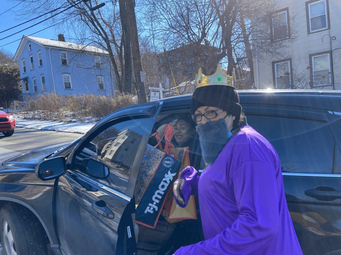 Person in a crown and purple robe gets out of car.