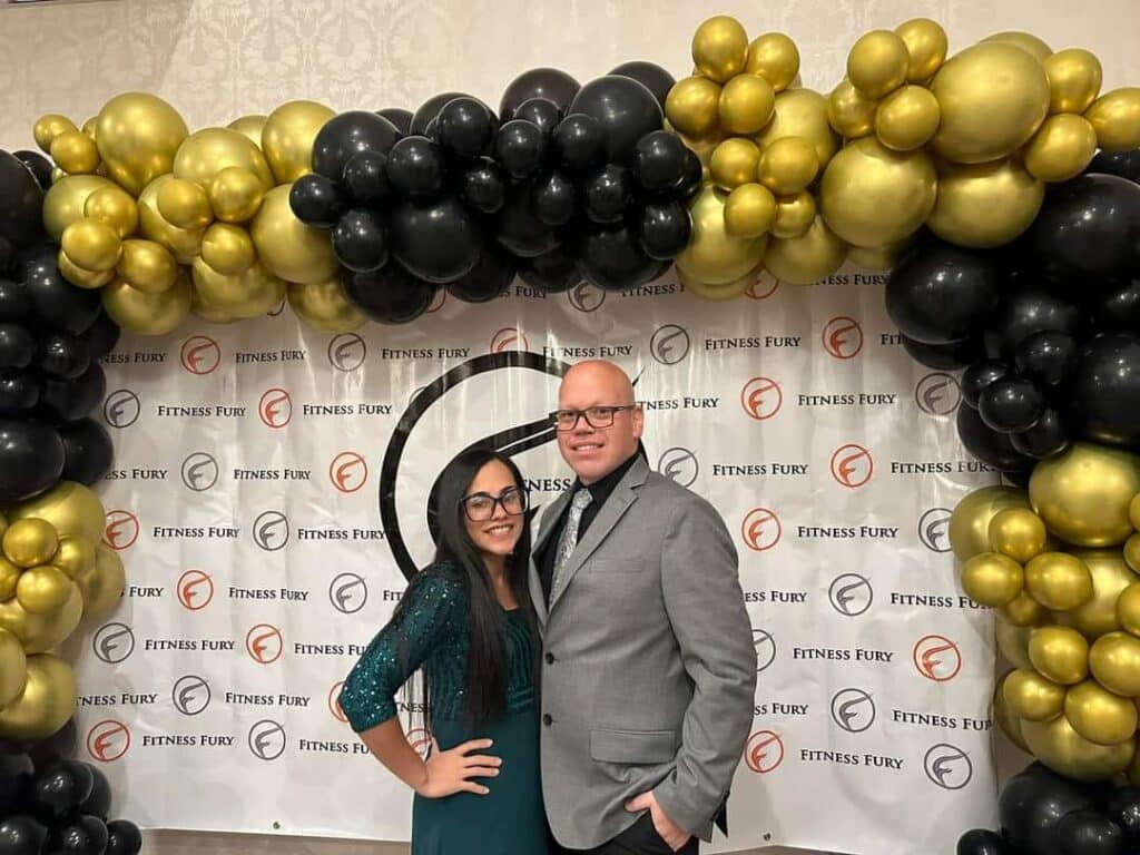 Couple posing in front of balloon arch.