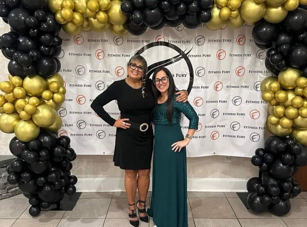 Two women posing for a picture in front of balloons.