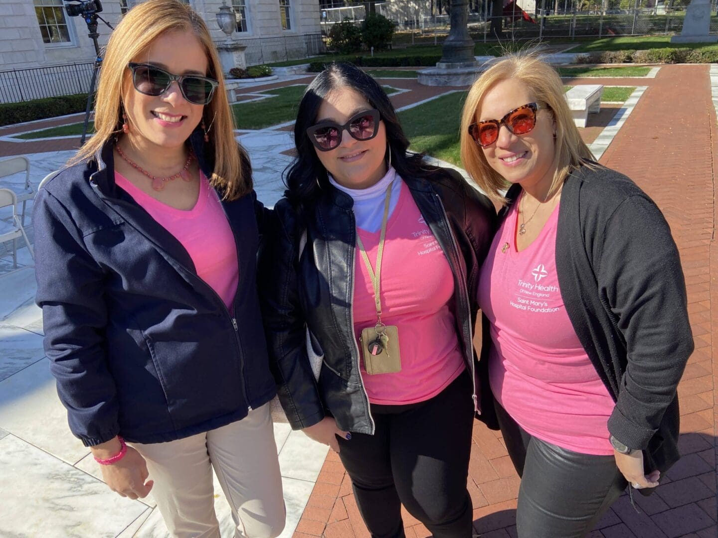 Three women wearing pink shirts and sunglasses.