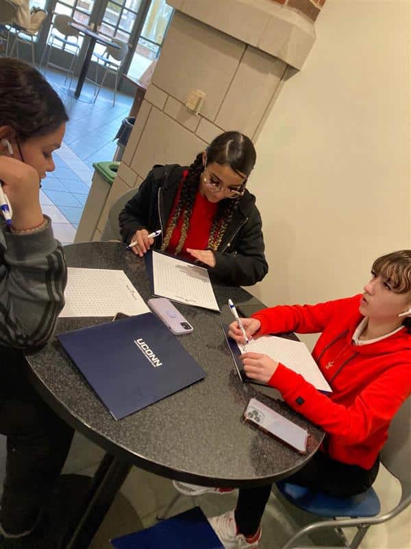 Three people sitting at a table writing on paper.