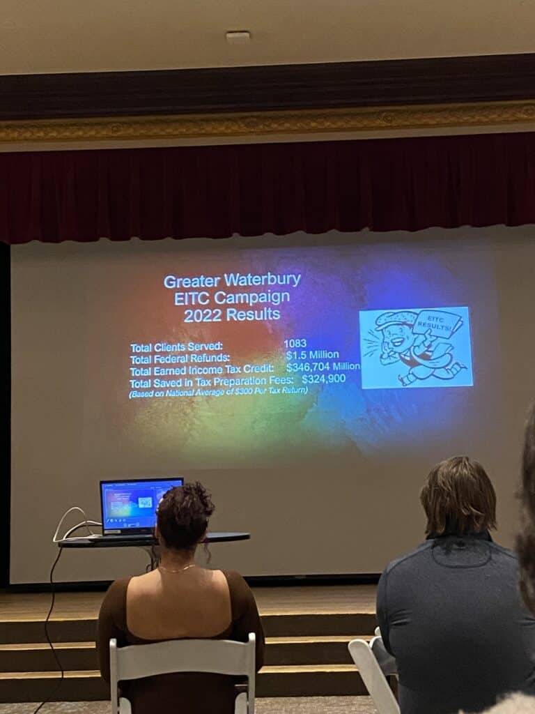 A group of people watching a presentation on a projector screen.