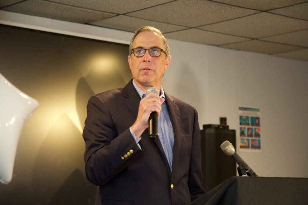 A man in suit and glasses holding a microphone.