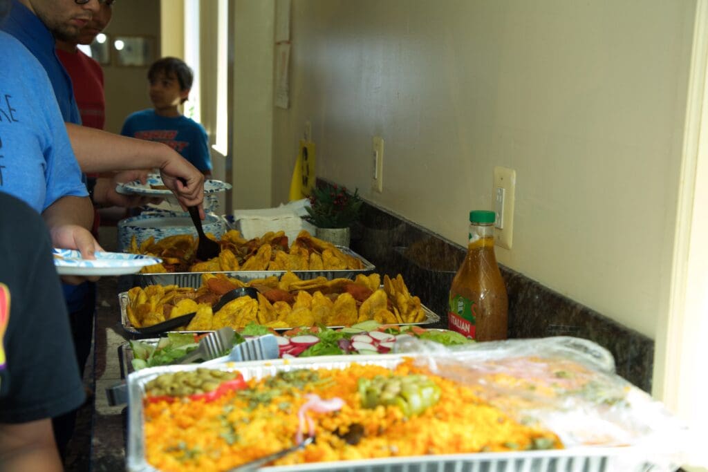 A buffet of food is shown with people in the background.