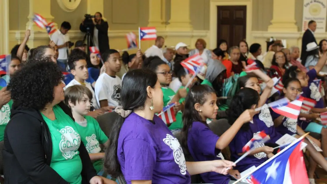 Attendees waving Puerto Rican flags inside Waterbury City Hall during the Mayor for a Day ceremony